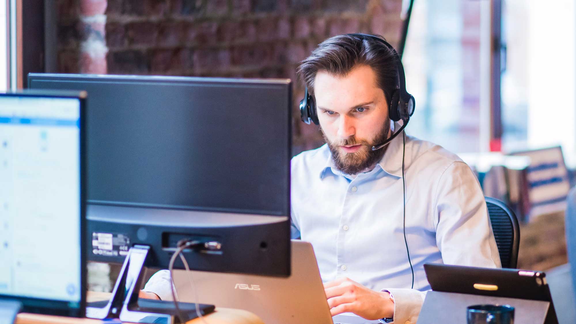 A man with headphones and microphone looking at computer
