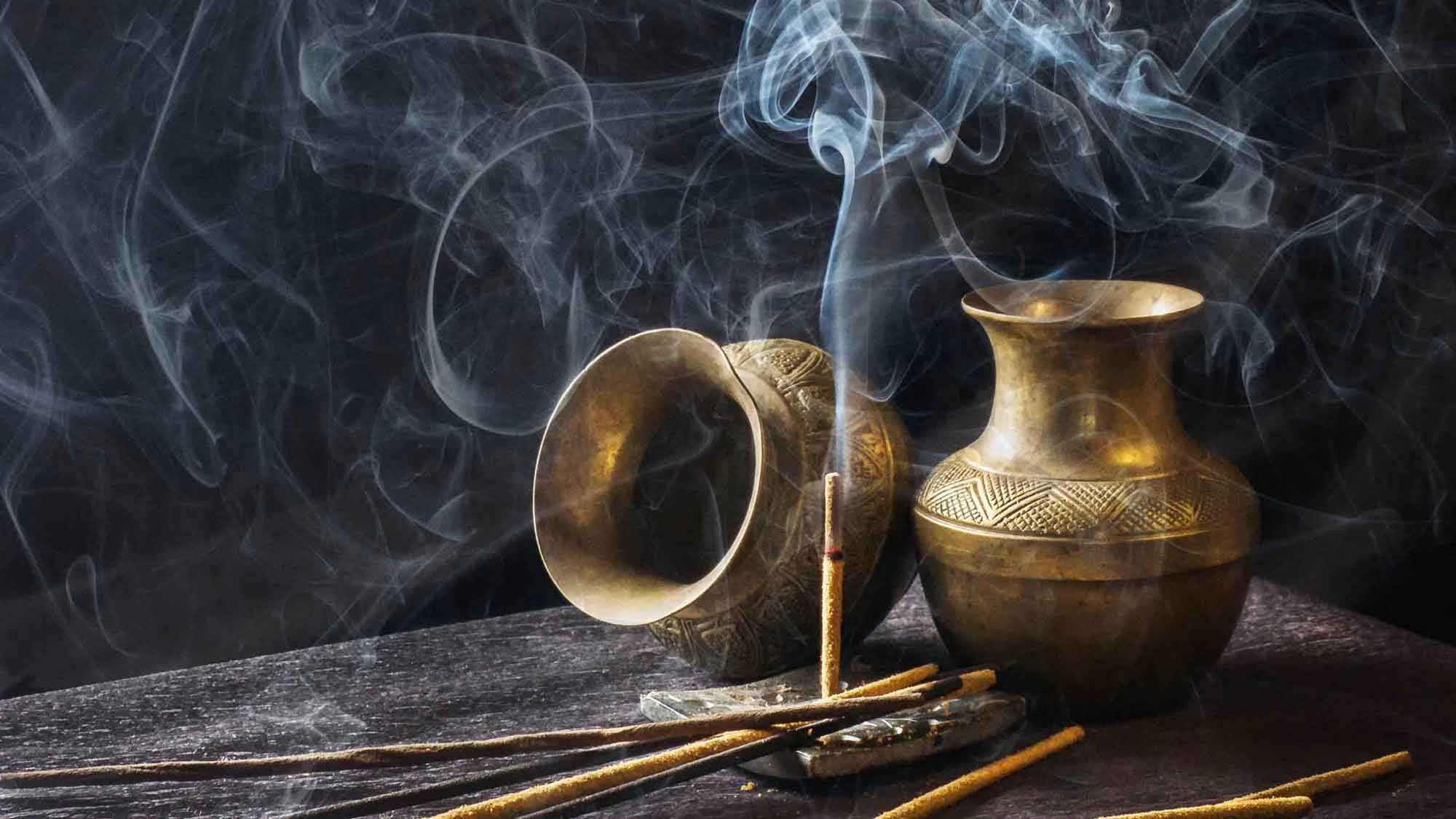 Two small golden jugs and a burning incense on a wooden table