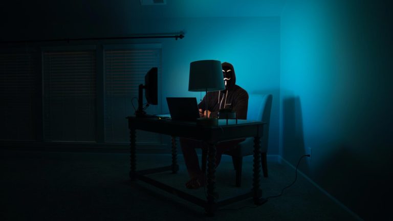 man at a computer disguised as an anonymous hacker in the dark